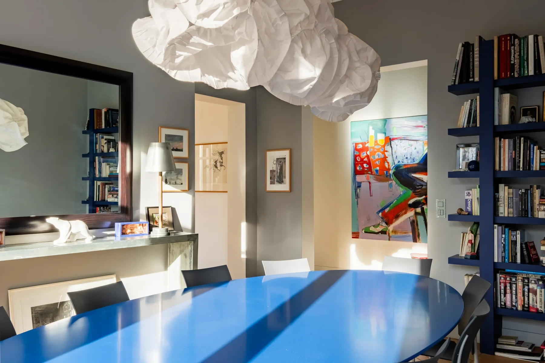 A dining area with a long blue table, bookshelves, and colorful artwork.