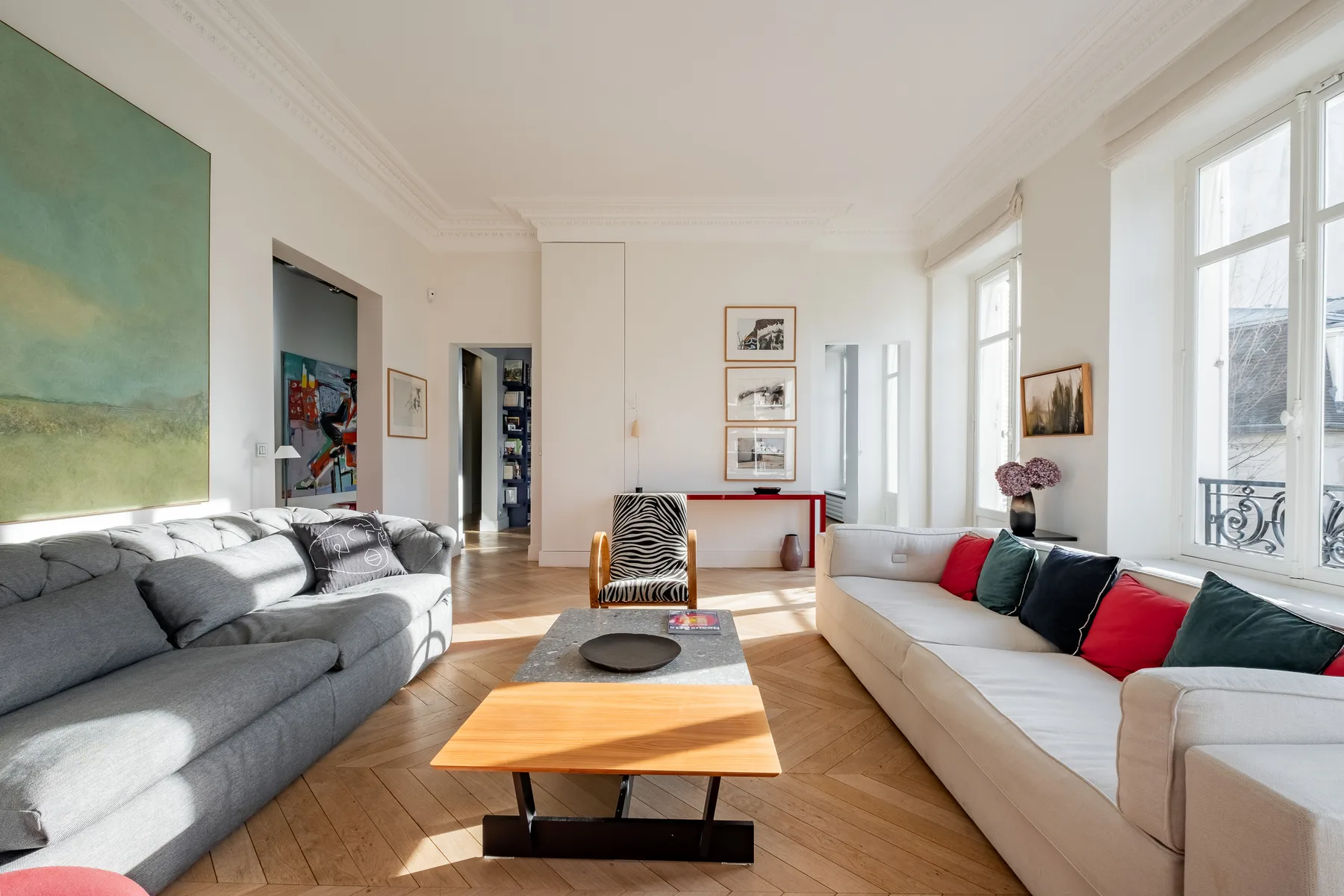 A bright living room with sofas, a coffee table, and tall windows.