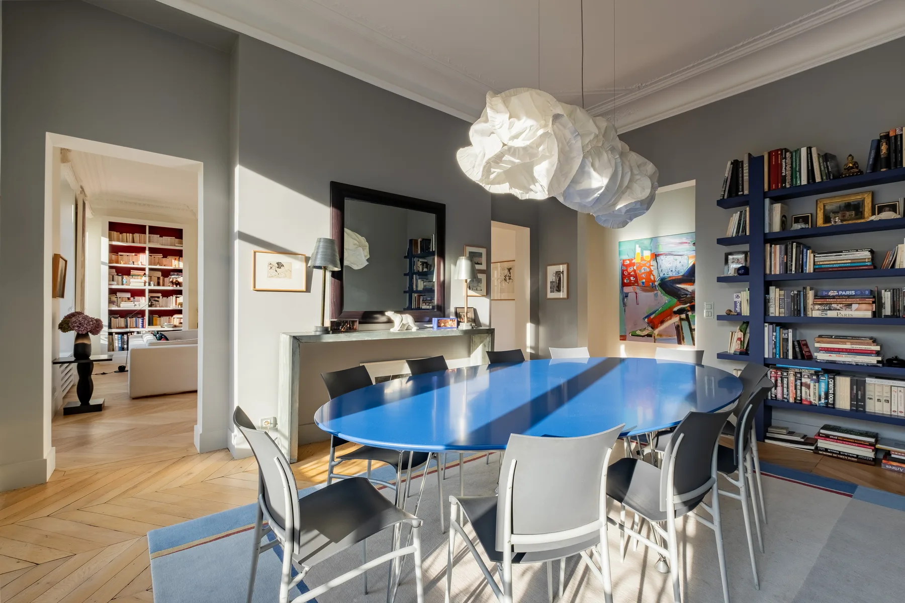 A dining room with a blue table, chairs, and a wall of bookshelves.