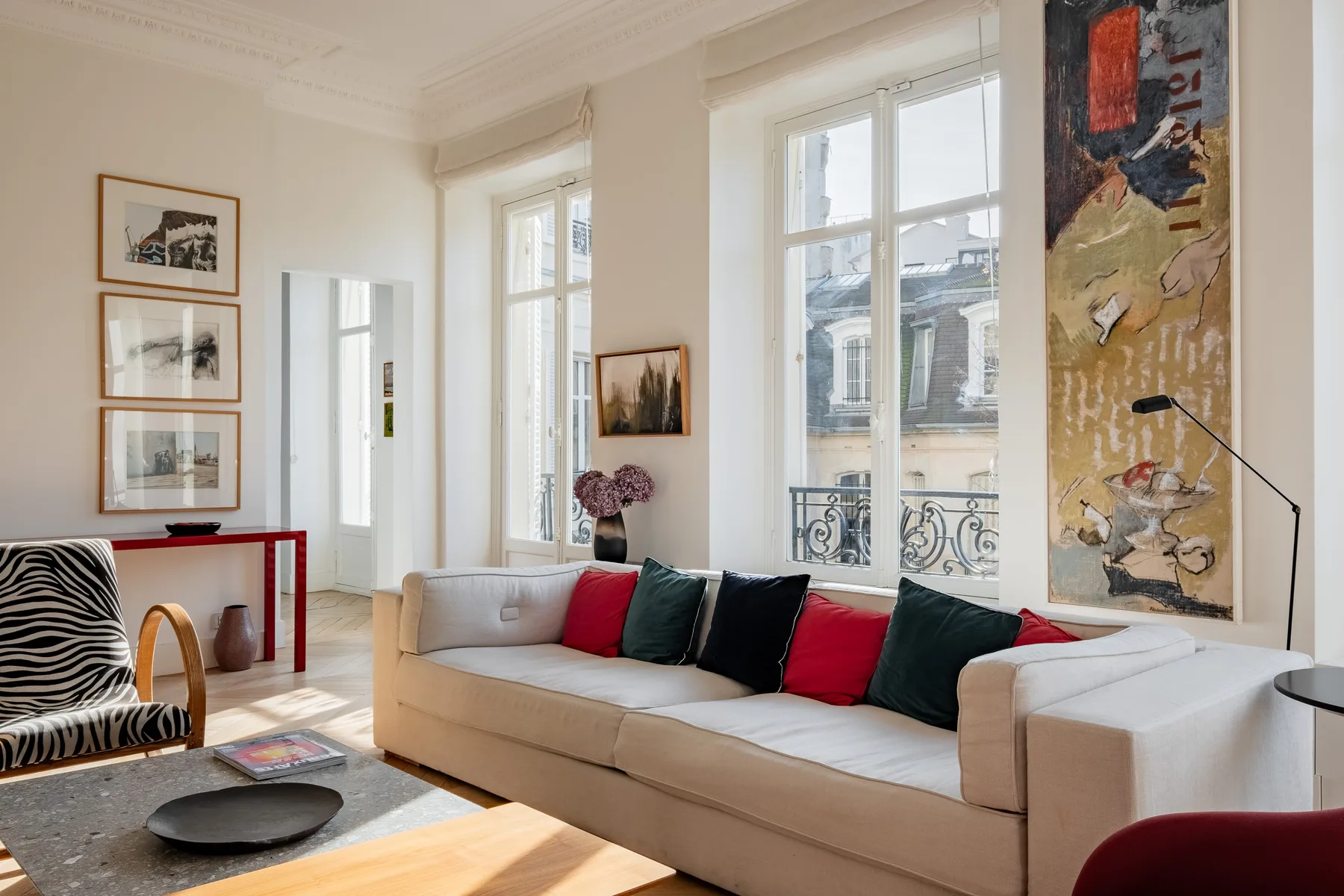 A bright living room with a long sofa, colorful cushions, and large windows.