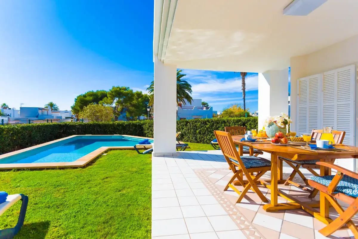 A covered patio with outdoor seating overlooks a swimming pool and garden.