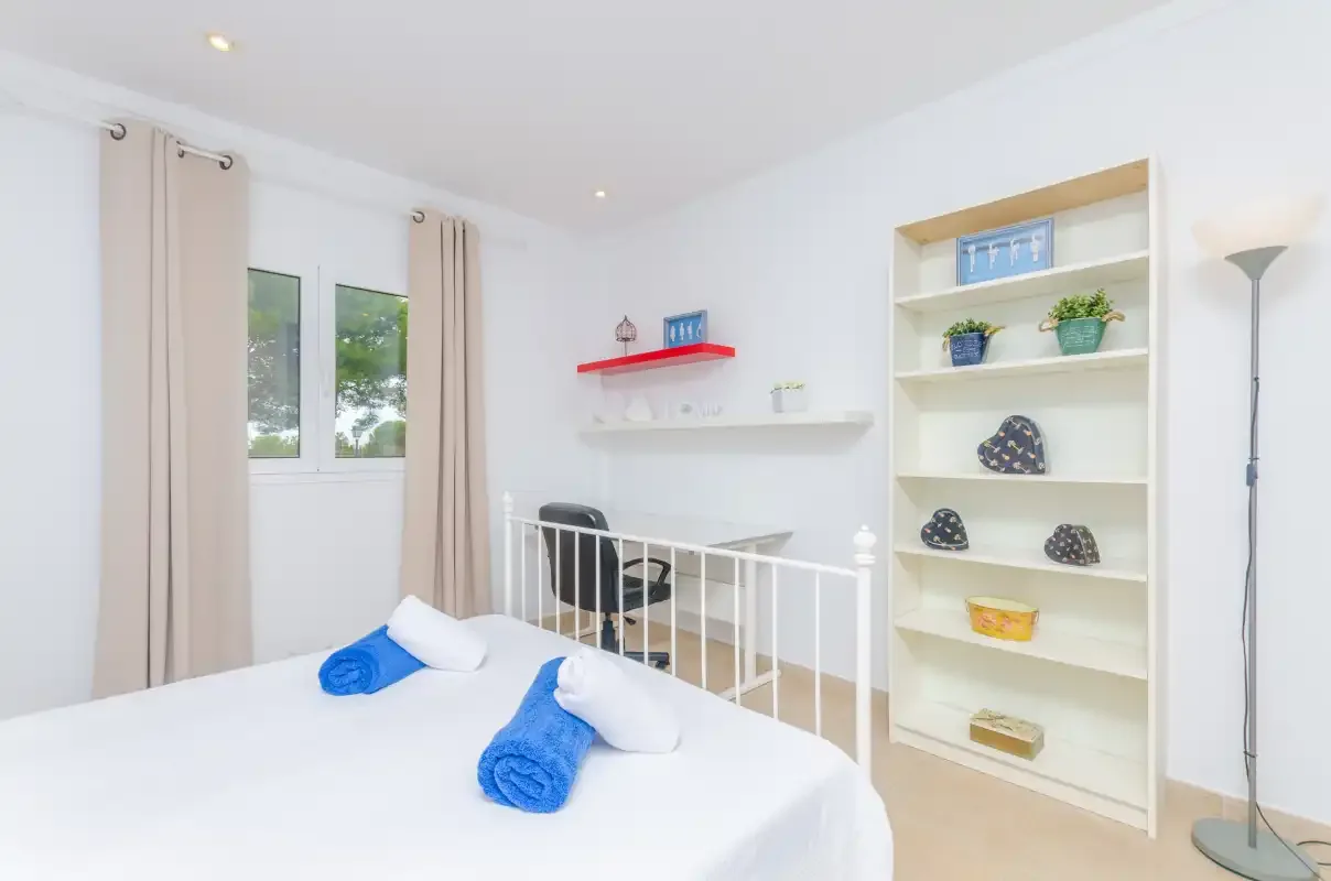A bright bedroom with a bed, window, and open shelving.