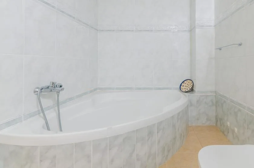 A tiled bathroom with a built-in bathtub and wall-mounted faucet.