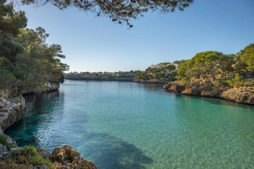 A clear turquoise cove is bordered by rocky, tree-covered shores.