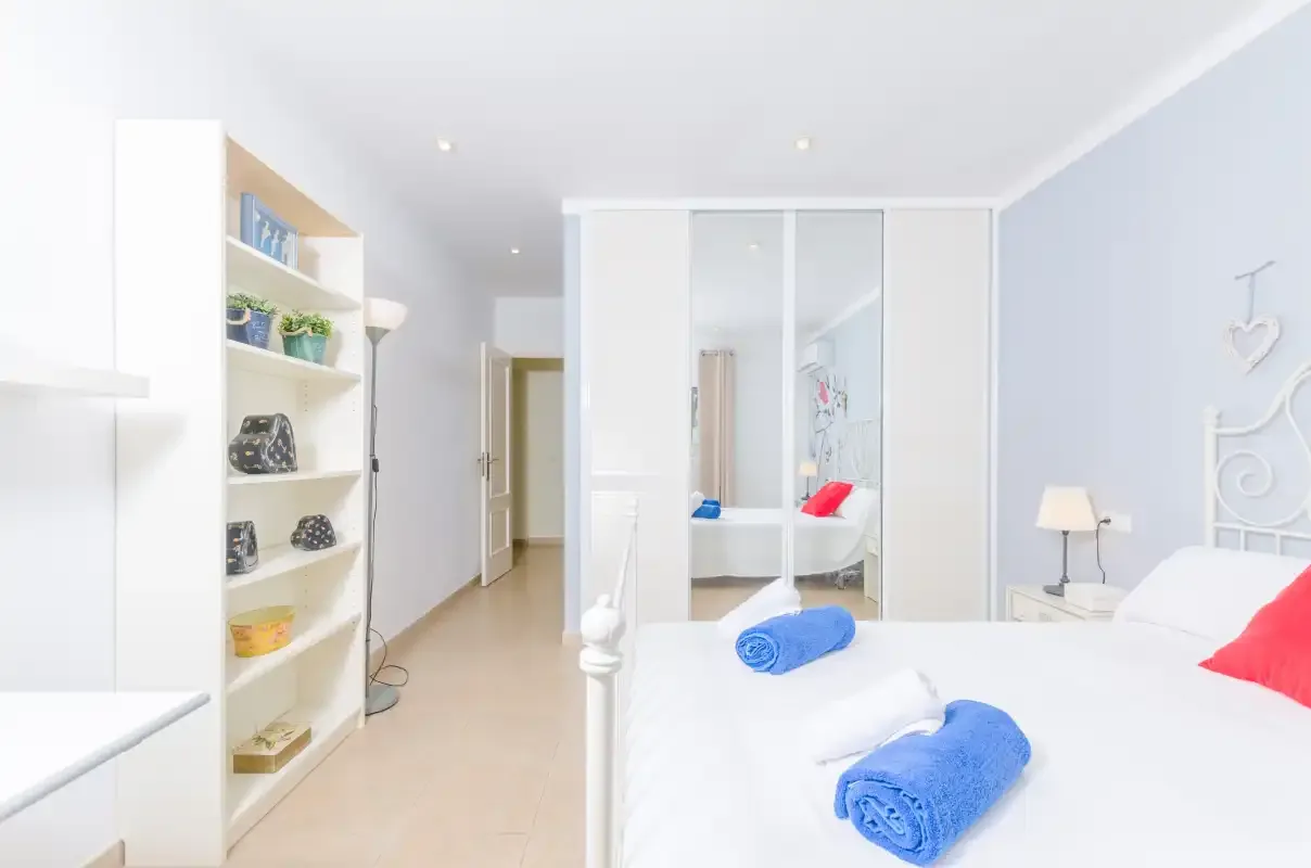 A bright bedroom with white bedding and built-in shelving.