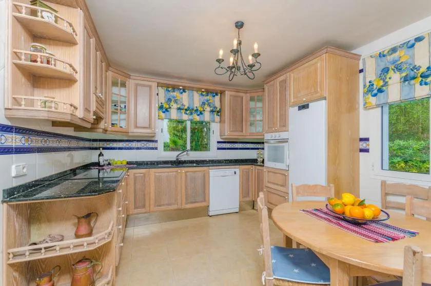 A bright kitchen with wooden cabinets, dark countertops, and a round dining table.