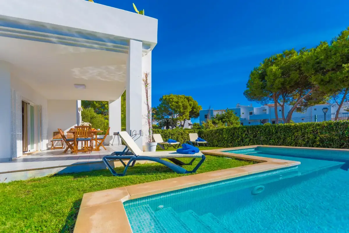 A modern white villa opens onto a swimming pool, lawn, and outdoor dining area.