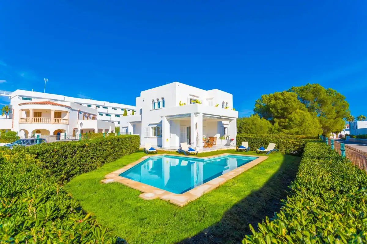 A white house stands beside a swimming pool and green lawn.