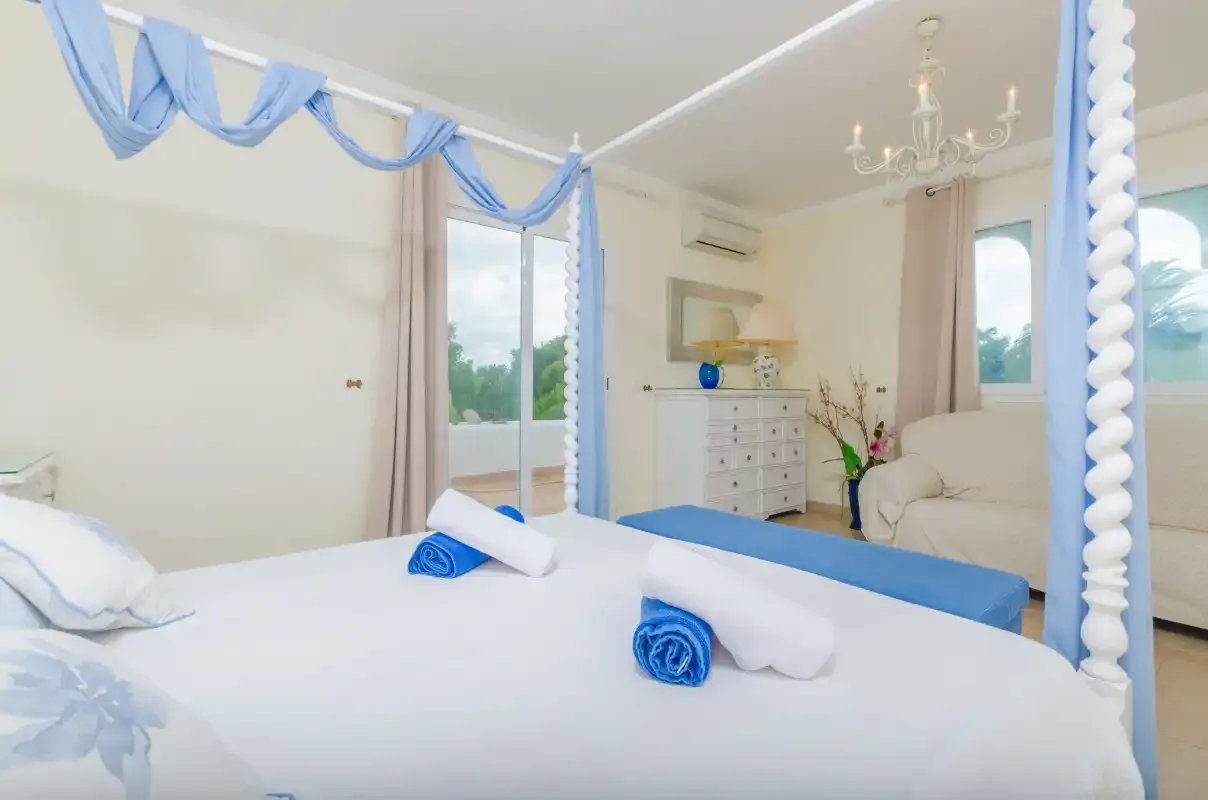 A bright bedroom with a canopy bed, blue drapes, and a white dresser.