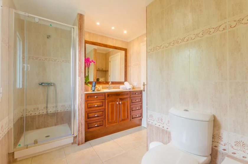 A tiled bathroom with a glass shower, wooden vanity, and toilet.