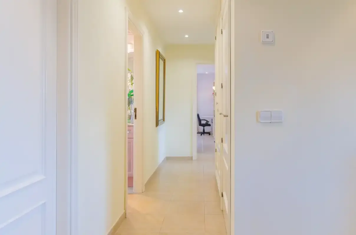 A bright hallway leads to a room with a desk and chair.
