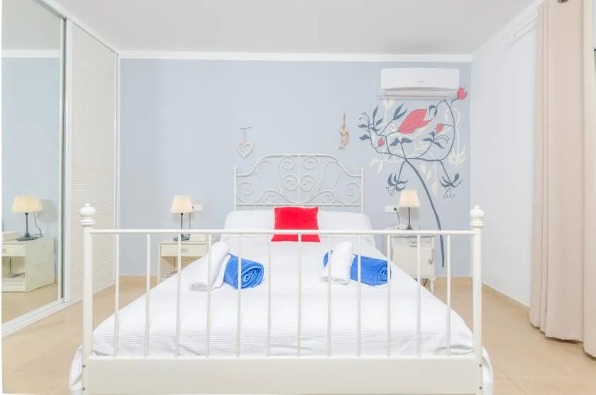A bright bedroom with a white bed and colorful floral wall art.