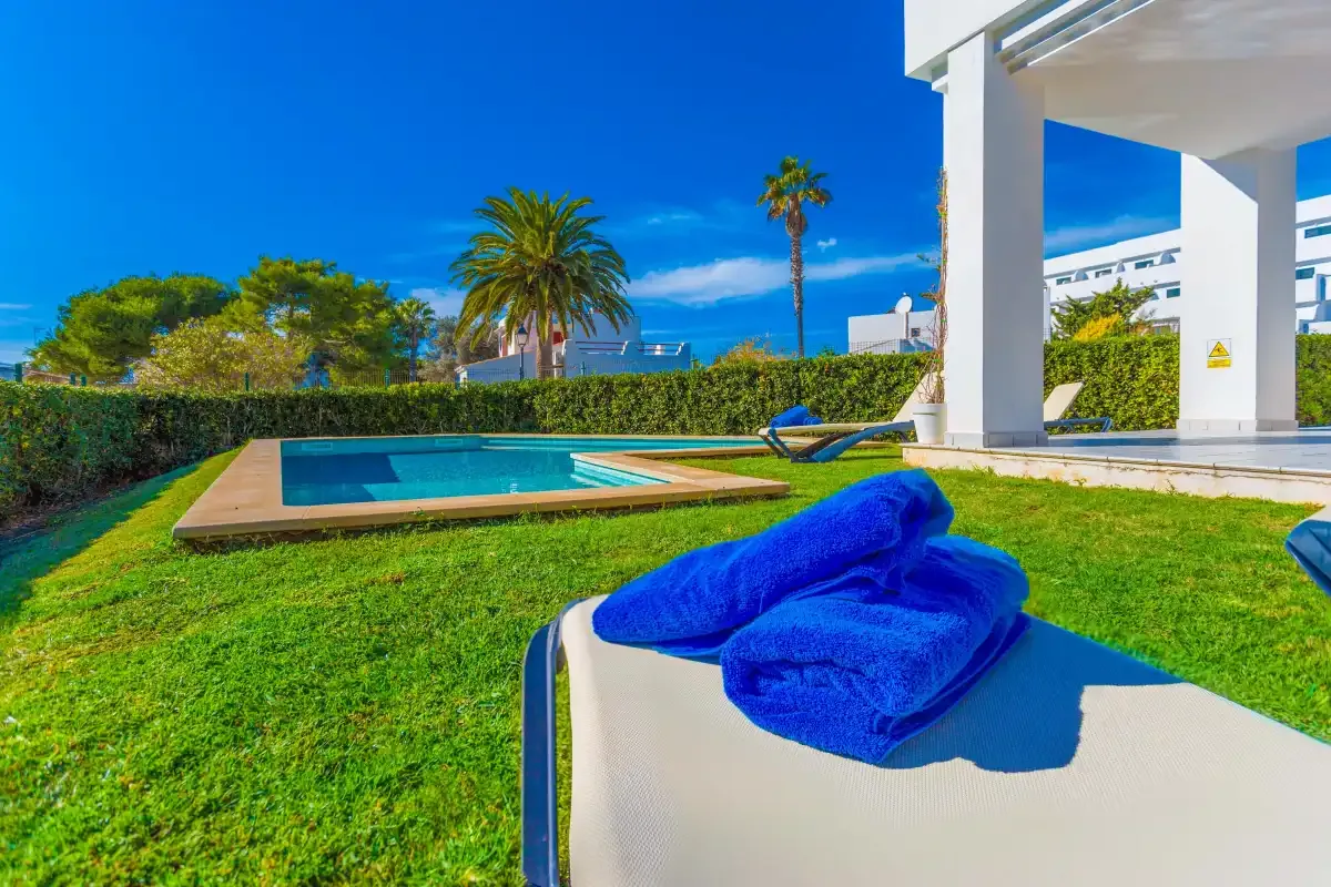 A pool beside a grassy lawn, with blue towels on a lounge chair.