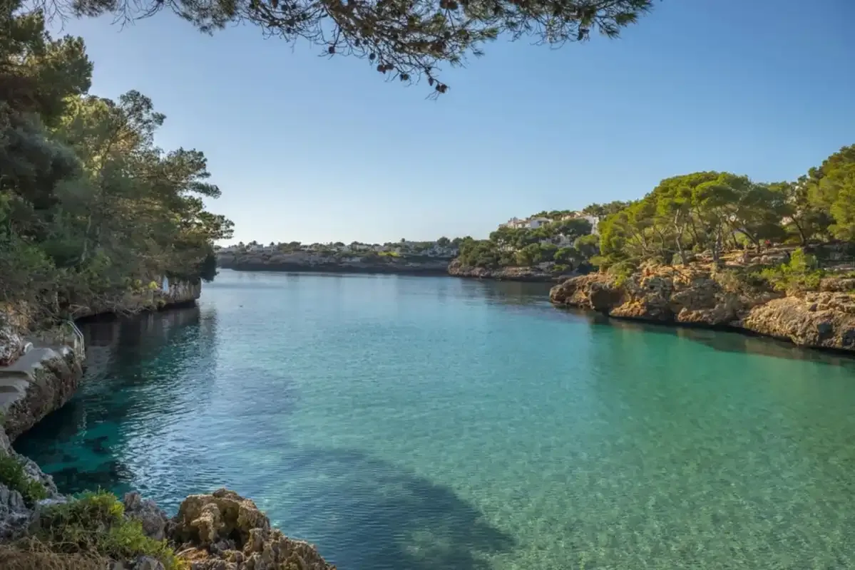A sheltered turquoise cove bordered by rocky, tree-covered shores.