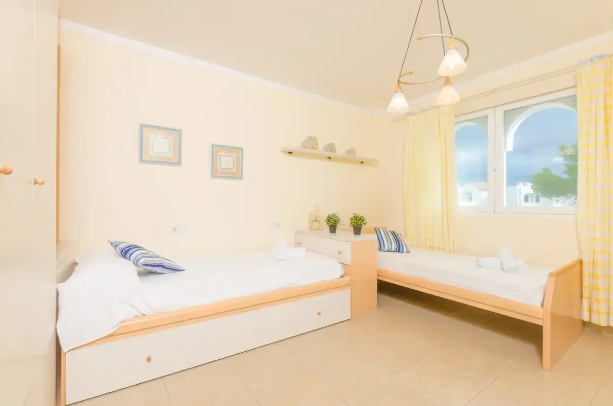 A bright bedroom with two beds and large windows.