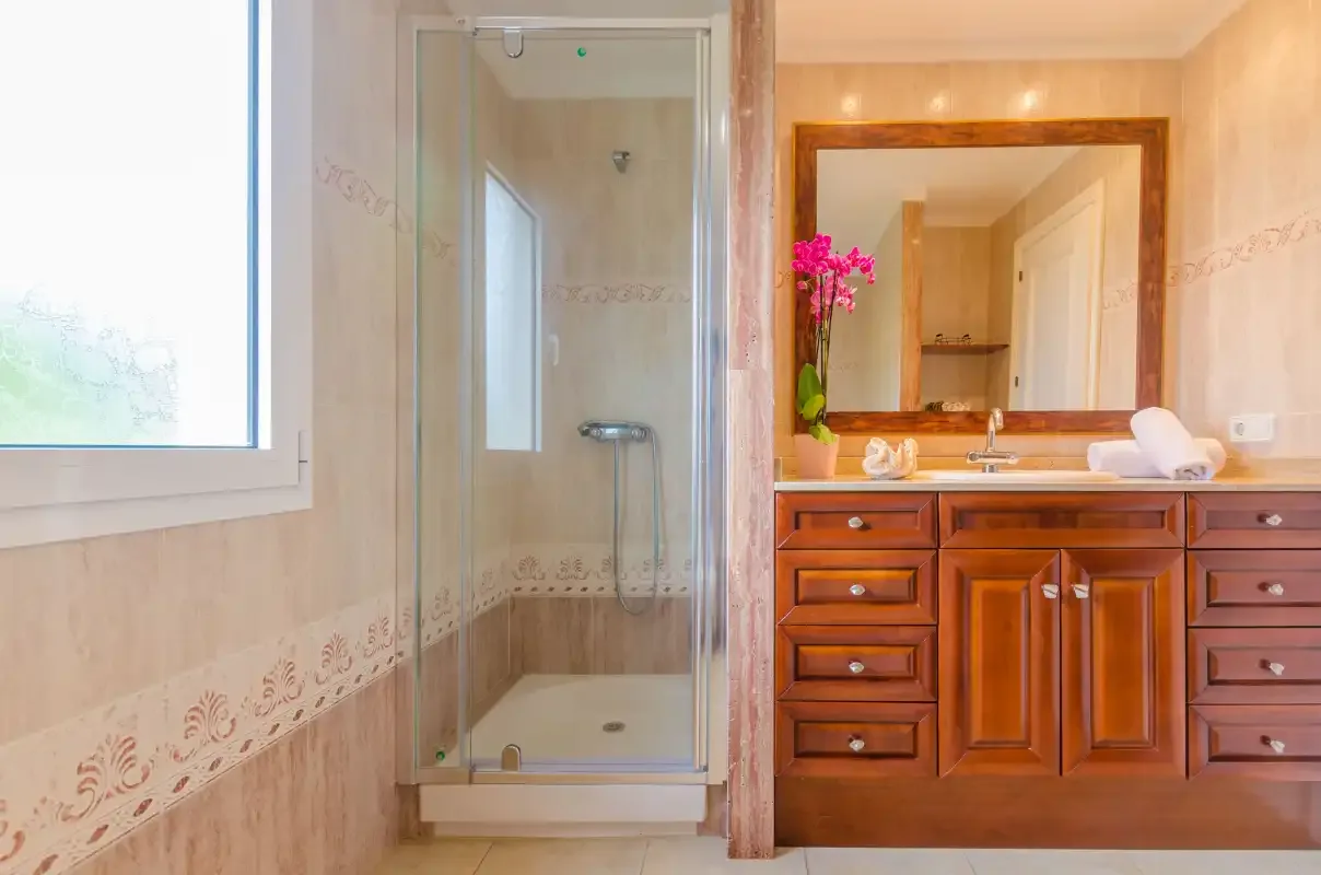 A bathroom with a glass shower and a wooden vanity beneath a mirror.