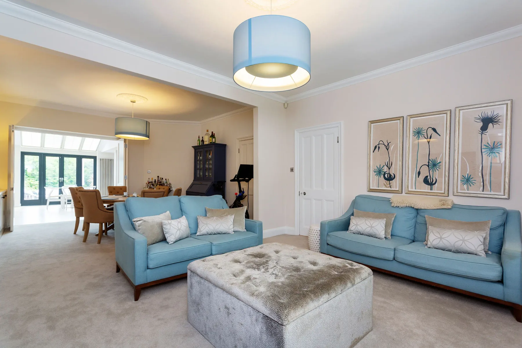 A bright living room with blue seating and framed botanical artwork.