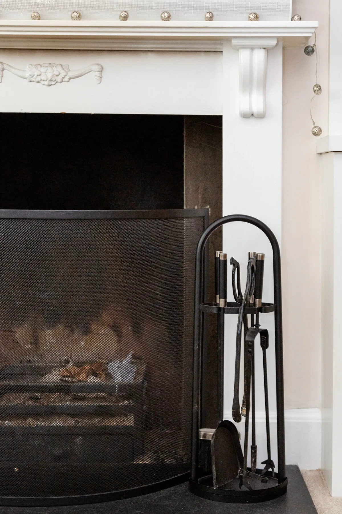 A fireplace with a dark screen and a set of fireplace tools beside it.