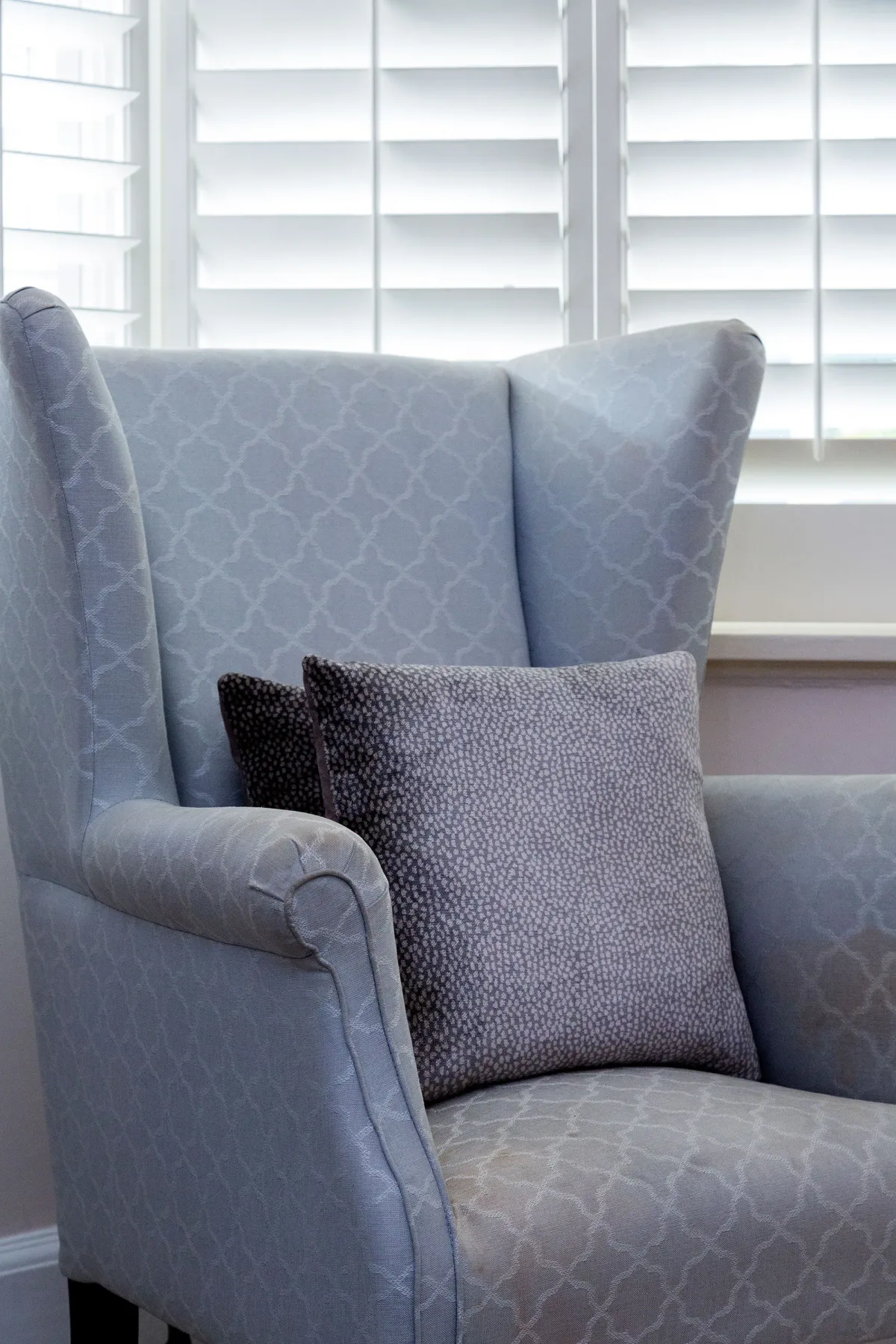 A blue upholstered armchair with patterned cushions sits in front of window blinds.