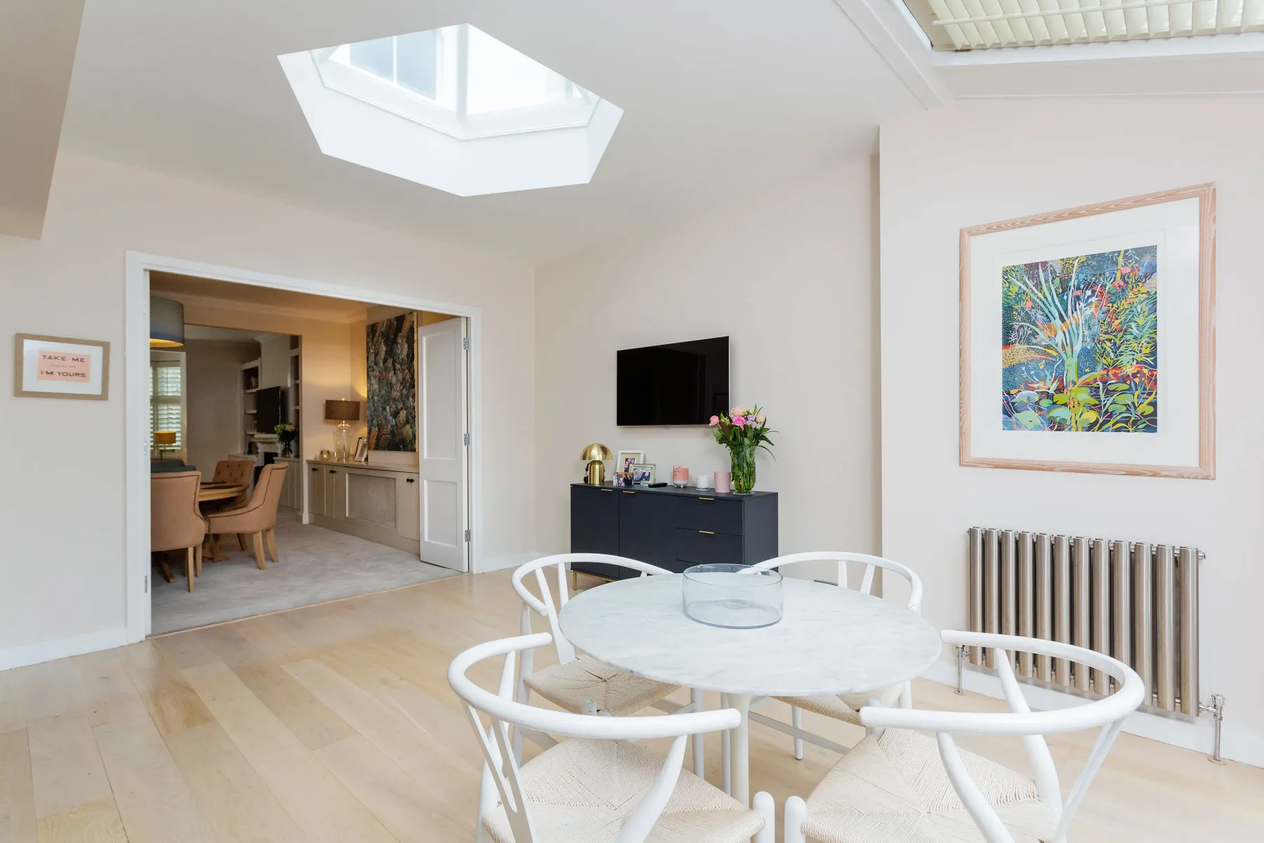 A dining area with a round table and chairs beside a framed artwork.