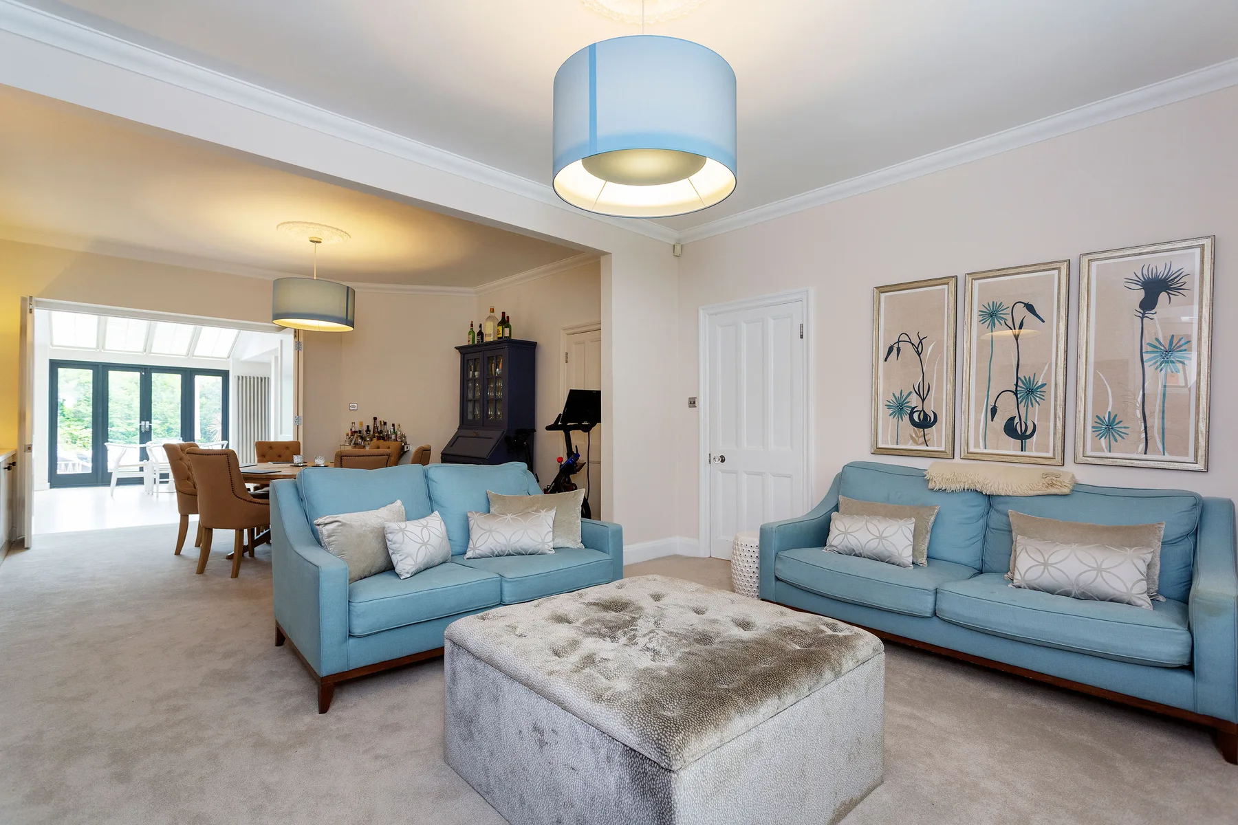 A living room with blue seating, a central ottoman, and framed wall art.
