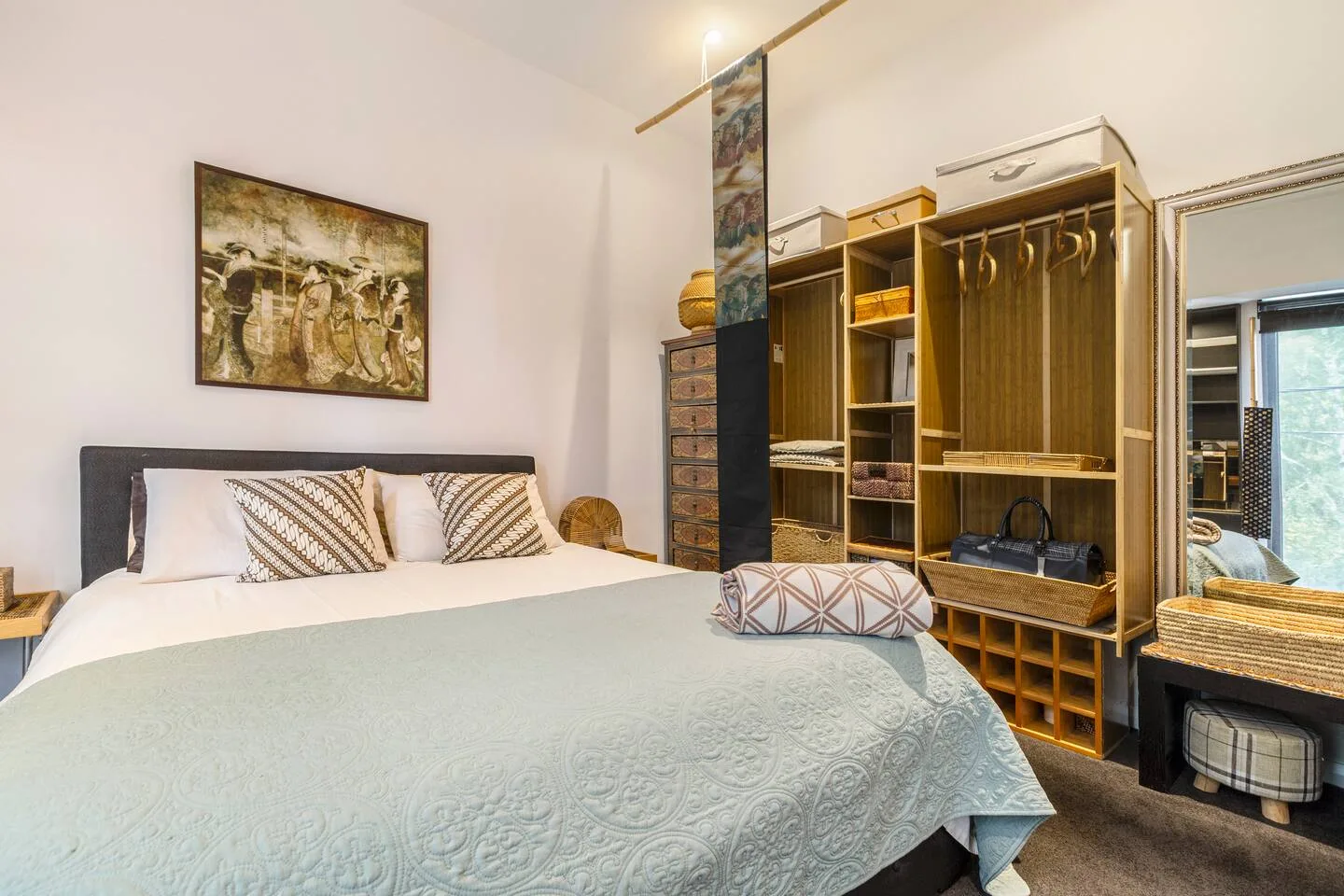 Un dormitorio con una cama bien tendida junto a almacenamiento abierto y estantes.