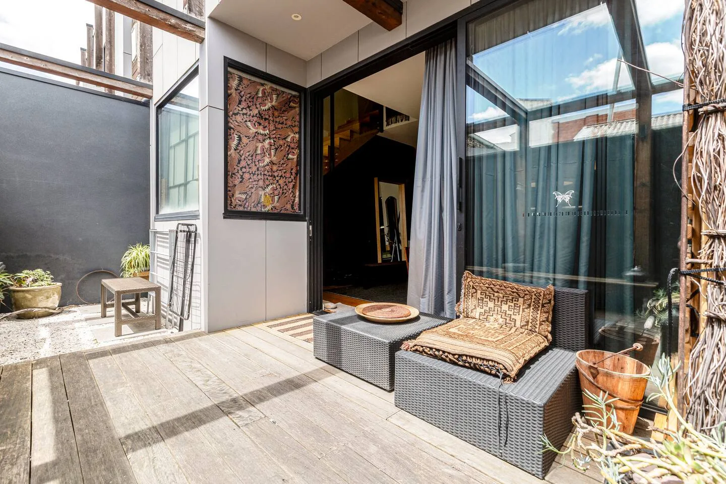 Un patio exterior junto a grandes puertas de vidrio tiene asientos tejidos y plantas en macetas.