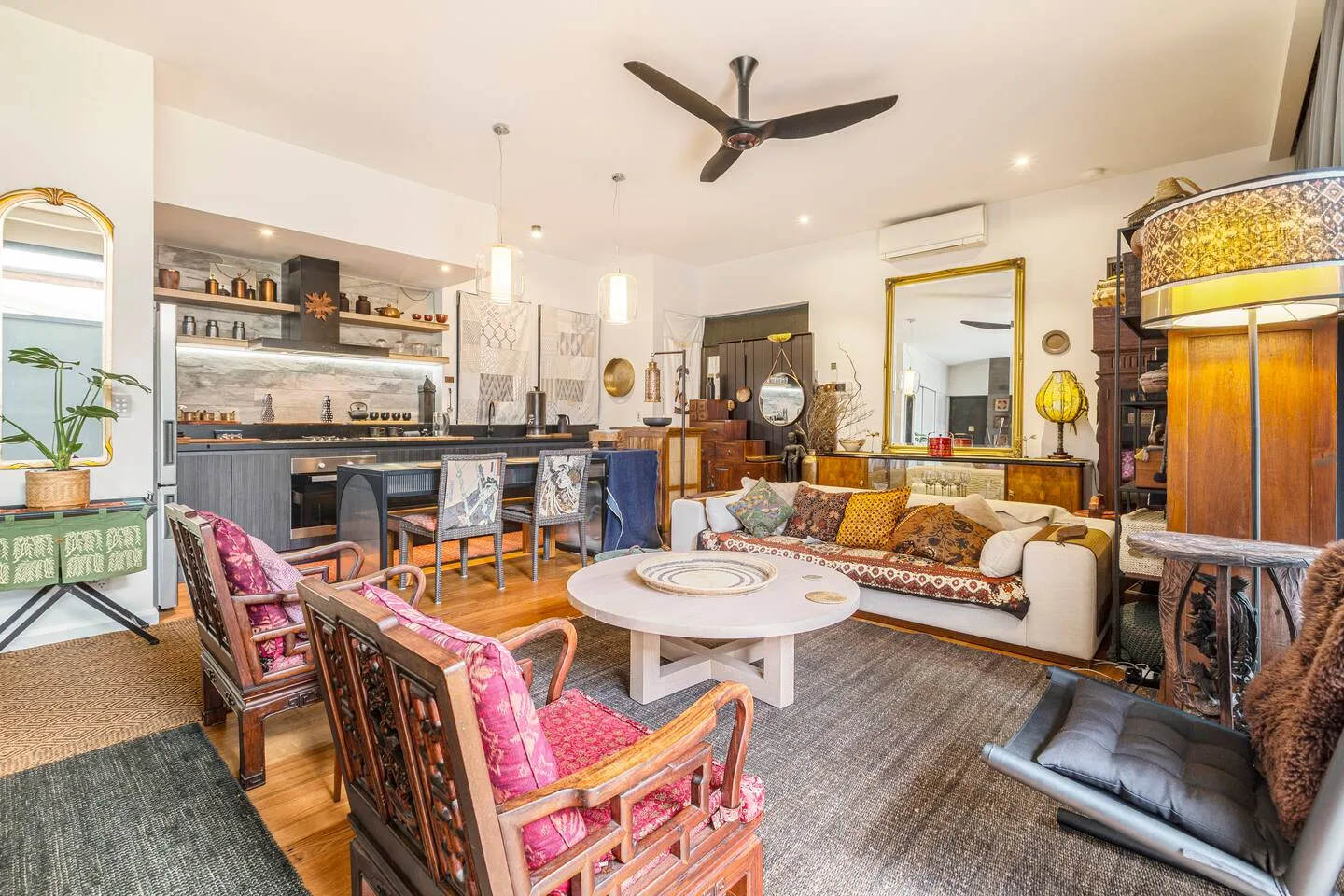 Una sala de estar luminosa tiene asientos alrededor de una mesa baja blanca, con un comedor al fondo.