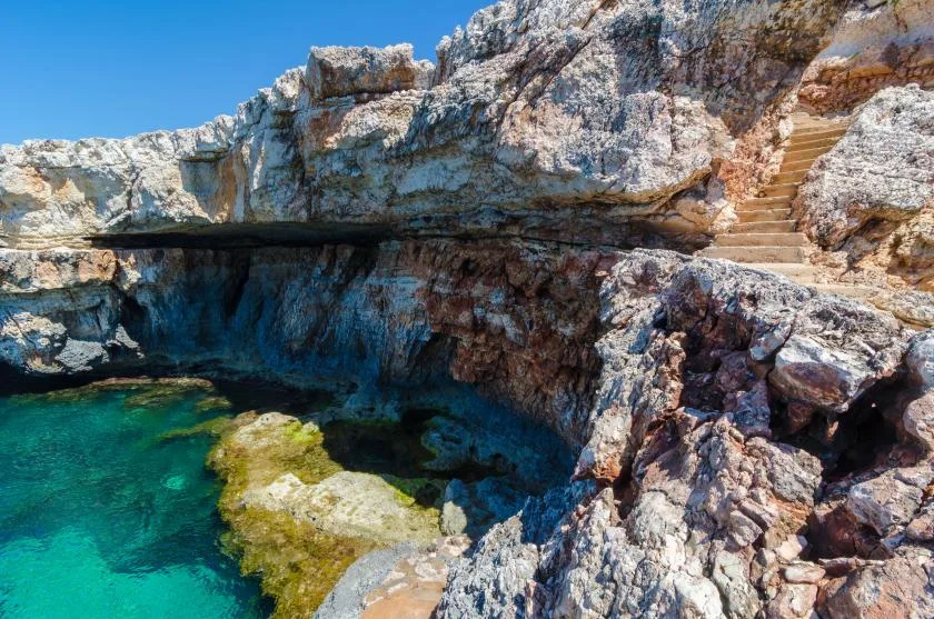 A rocky coastal inlet with clear turquoise water and stone steps along the cliff.