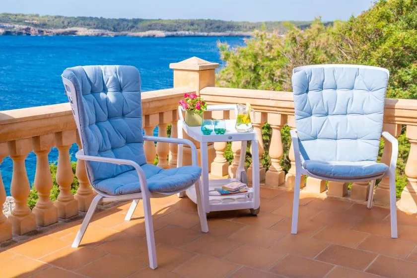 Two cushioned chairs and a small table sit on a terrace overlooking the sea.