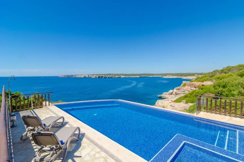 Una piscina al aire libre da a un mar azul, con asientos junto a ella.