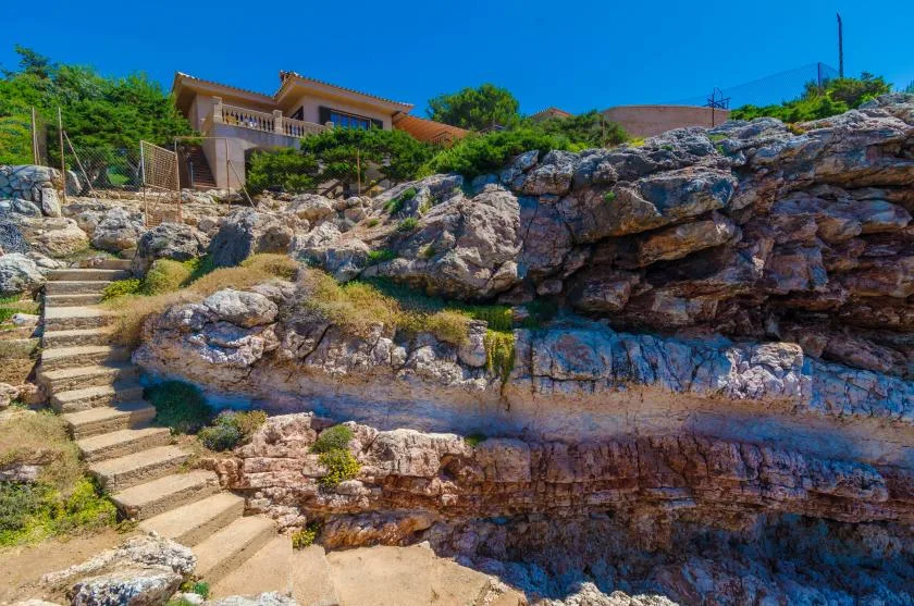 A rocky hillside path with stone steps leads toward a house above.