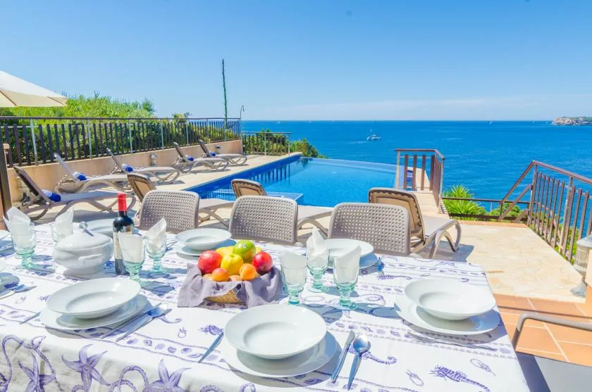 Una mesa de comedor junto a la piscina está puesta en una terraza con vistas al mar.