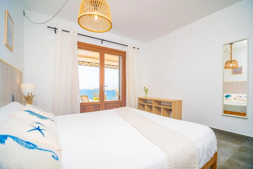 A bright bedroom with a white bed and glass doors opening onto a balcony.