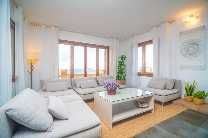 A bright living room with light-colored seating around a glass coffee table.