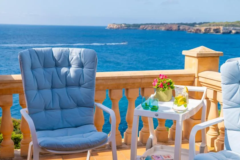 A seaside balcony with cushioned seating and a small table overlooking the water.