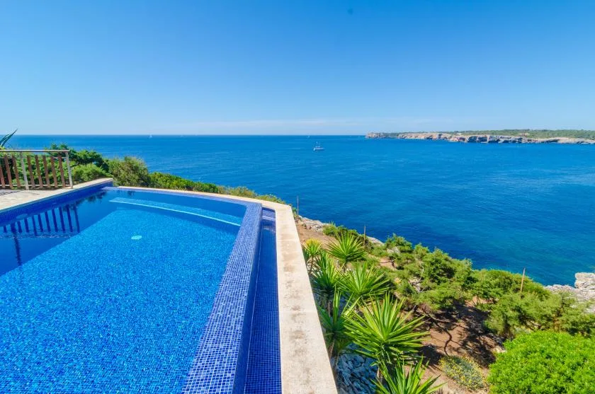 A swimming pool overlooks the blue sea and green coastal vegetation.