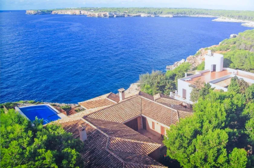 Aerial view of a coastal house with tiled roofs beside a deep blue bay.