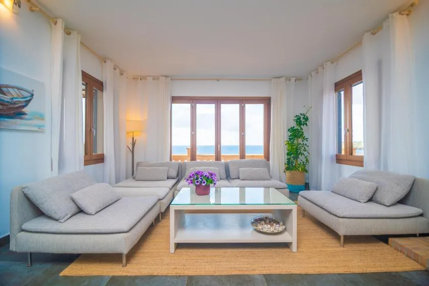 A bright living room with seating around a glass coffee table and ocean views.