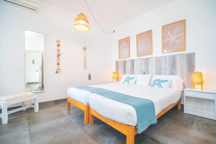 A bright bedroom with two beds arranged side by side beneath framed wall art.