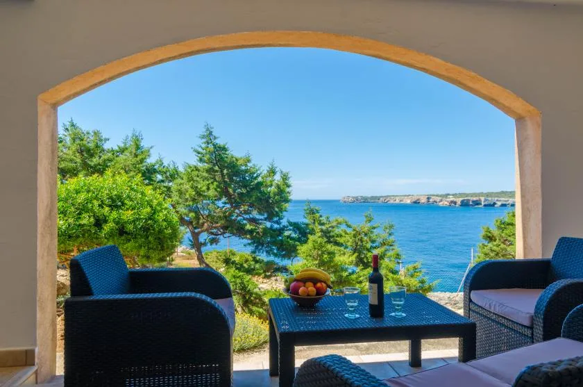 Una abertura arqueada enmarca asientos al aire libre y una mesa con vistas al mar.