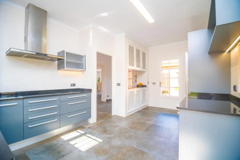 A bright modern kitchen with blue cabinetry, a range hood, and a sunlit window.