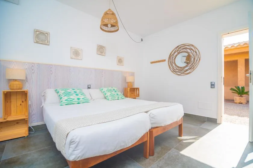 A bedroom with two beds, green patterned pillows, and a woven pendant light.
