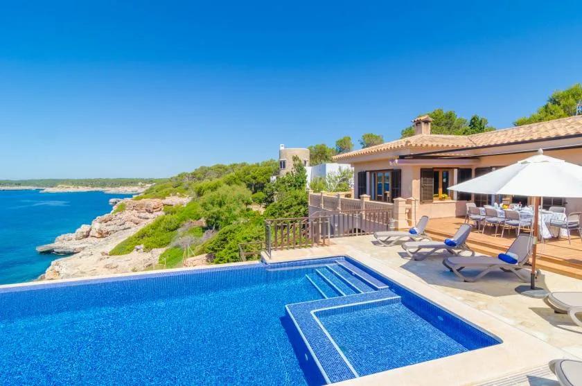A seaside patio overlooks a blue pool and rocky coastline.