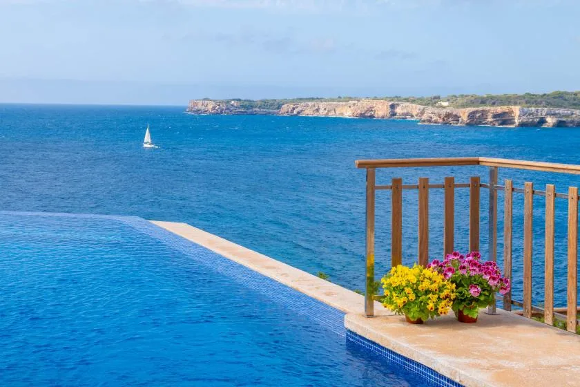 A swimming pool overlooks the blue sea, with flowers beside the railing.