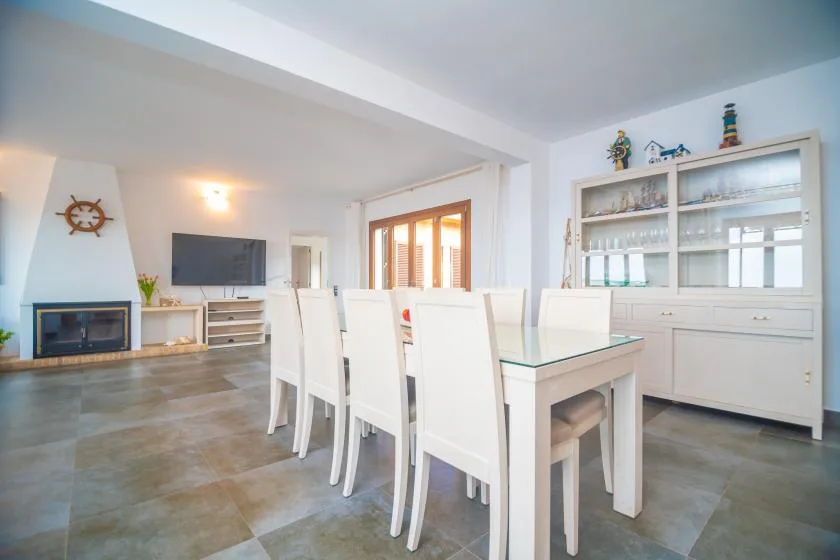 A dining area with white seating, a glass-topped table, and a display cabinet.
