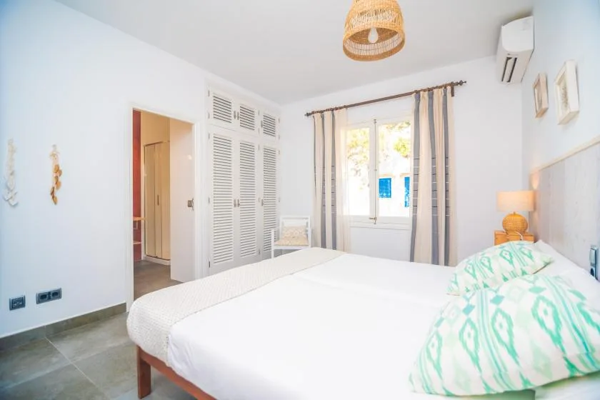 A bright bedroom with a large bed, shuttered closets, and a curtained window.