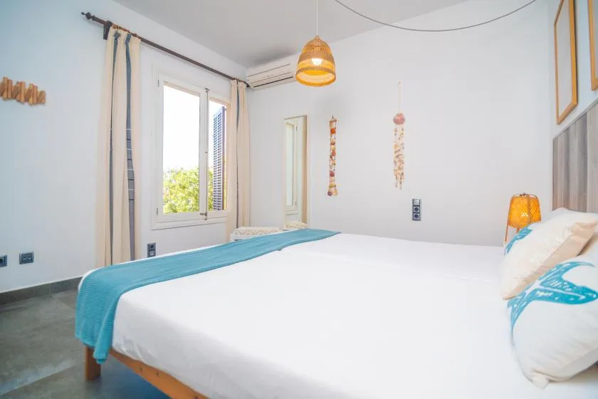 A bright bedroom with a white bed and a window overlooking greenery.