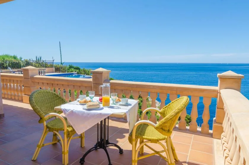 A terrace dining table is set beside a balustrade overlooking the sea.