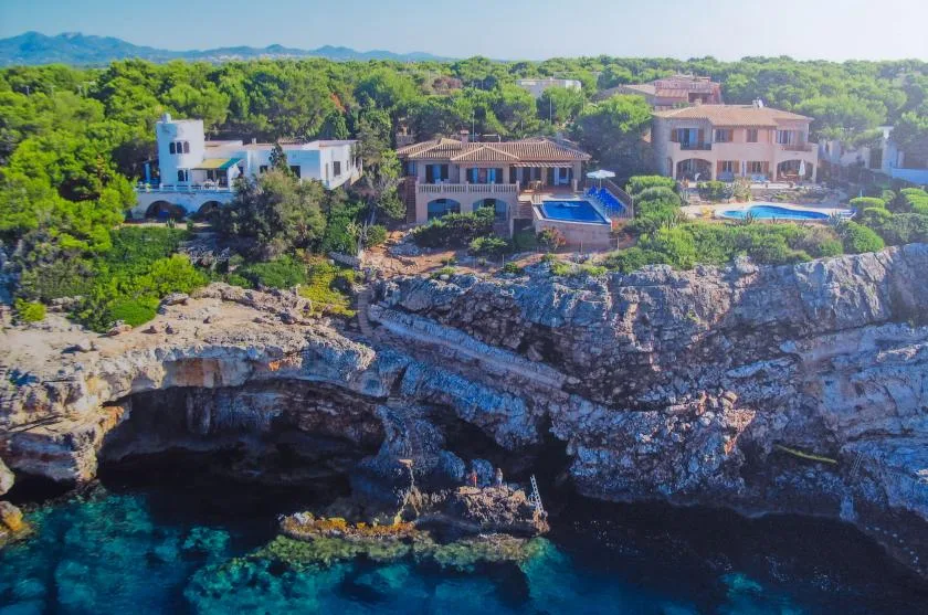 Aerial view of seaside buildings and pools above a rocky shoreline.